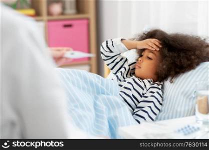 healthcare, medicine and people concept - doctor with thermometer measuring temperature of little sick african american girl lying in bed at home. doctor measuring sick girl&rsquo;s temperature