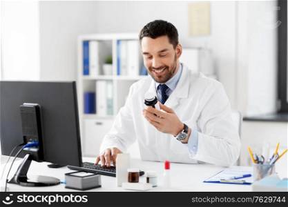 healthcare, medicine and people concept - happy smiling male doctor with drug in jar and computer at hospital. male doctor with medicine and computer at hospital