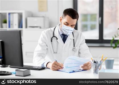 healthcare, medicine and people concept - male doctor in medical mask with clipboard at hospital. smiling male doctor with clipboard at hospital