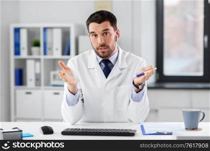 healthcare, medicine and people concept - male doctor with earphones having video conference at hospital. doctor in earphones having video call at clinic