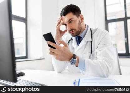 healthcare, medicine and people concept - male doctor with smartphone at hospital. male doctor with smartphone at hospital