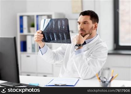 healthcare, medicine and people concept - male doctor with x-ray of spine at hospital. male doctor with x-ray of spine at hospital