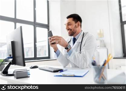 healthcare, medicine and people concept - smiling male doctor with smartphone at hospital. smiling male doctor with smartphone at hospital
