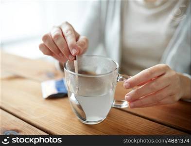 healthcare, medicine and people concept - woman stirring medication in cup of water with spoon