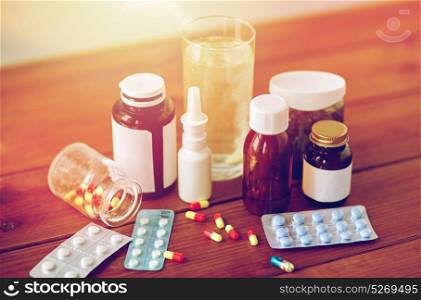 healthcare, medicine and pharmaceutical drugs concept - pills, nasal spray, antipyretic syrup and glass on wooden table. medicine and drugs on wooden table