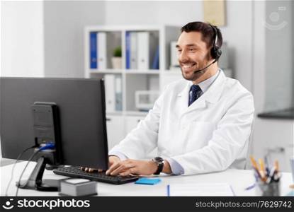 healthcare, medicine and technology concept - happy smiling male doctor with computer and headset working at hospital. happy doctor with computer and headset at hospital