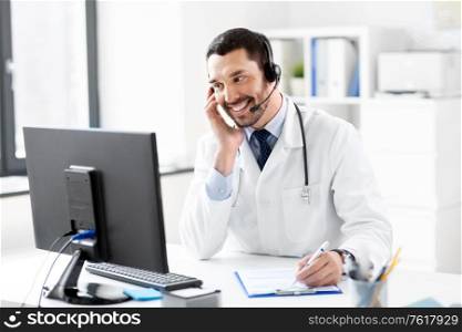 healthcare, medicine and technology concept - happy smiling male doctor with headset, computer and clipboard working at hospital. happy doctor with computer and headset at hospital
