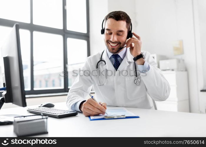 healthcare, medicine and technology concept - happy smiling male doctor with headset, computer and clipboard working at hospital. happy doctor with computer and headset at hospital