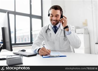 healthcare, medicine and technology concept - happy smiling male doctor with headset, computer and clipboard working at hospital. happy doctor with computer and headset at hospital