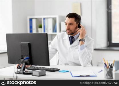 healthcare, medicine and technology concept - male doctor with computer and headset working at hospital. male doctor with computer and headset at hospital