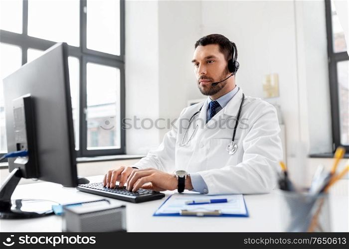 healthcare, medicine and technology concept - male doctor with computer and headset working at hospital. male doctor with computer and headset at hospital