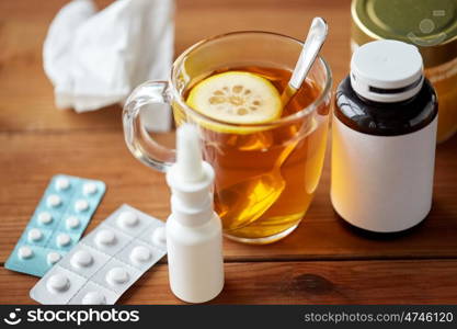healthcare, medicine and treatment concept - cup of tea, drugs, honey and paper tissue on wooden table