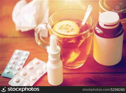healthcare, medicine and treatment concept - cup of tea, drugs, honey and paper tissue on wooden table. cup of tea, drugs, honey and paper tissue on wood