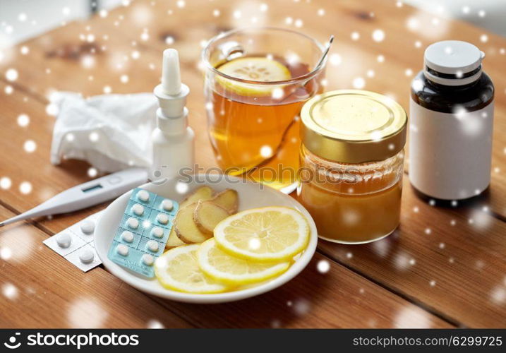 healthcare, medicine and treatment concept - drugs, thermometer, honey and cup of tea on wooden table over snow. drugs, thermometer, honey and cup of tea on wood