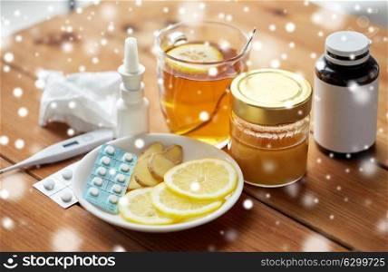 healthcare, medicine and treatment concept - drugs, thermometer, honey and cup of tea on wooden table over snow. drugs, thermometer, honey and cup of tea on wood