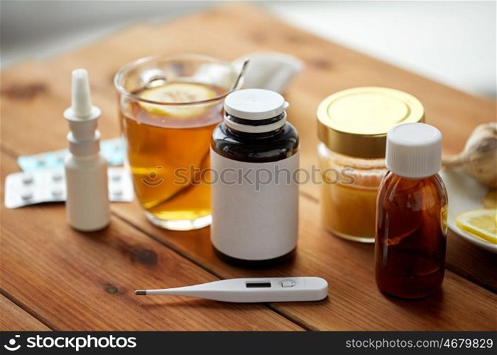healthcare, medicine and treatment concept - drugs, thermometer, honey and cup of tea on wooden table