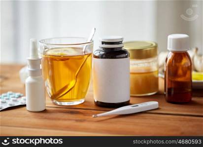 healthcare, medicine and treatment concept - drugs, thermometer, honey and cup of tea on wooden table