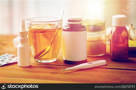 healthcare, medicine and treatment concept - drugs, thermometer, honey and cup of tea on wooden table. drugs, thermometer, honey and cup of tea on wood