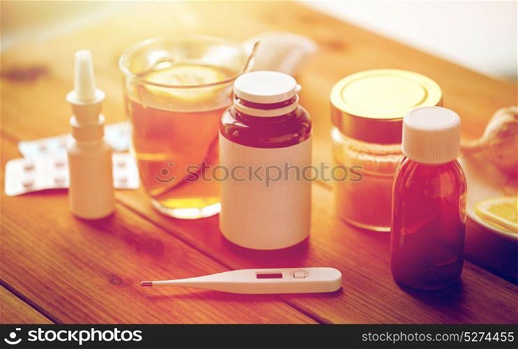 healthcare, medicine and treatment concept - drugs, thermometer, honey and cup of tea on wooden table. drugs, thermometer, honey and cup of tea on wood