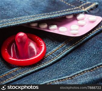 Healthcare medicine, contraception and birth control. Closeup oral contraceptive pills, red condom on denim pocket background