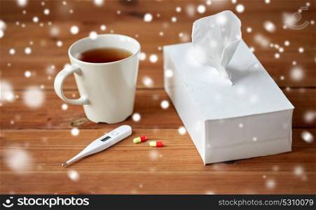 healthcare, medicine, flu and treatment concept - cup of tea, paper wipes and thermometer with pills over snow. cup of tea, paper wipes and thermometer with pills