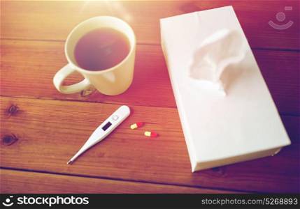 healthcare, medicine, flu and treatment concept - cup of tea, paper wipes and thermometer with pills. cup of tea, paper wipes and thermometer with pills