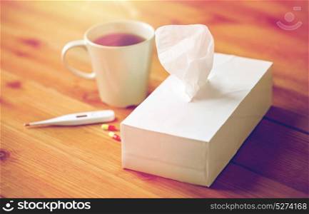 healthcare, medicine, flu and treatment concept - cup of tea, paper wipes and thermometer with pills. cup of tea, paper wipes and thermometer with pills