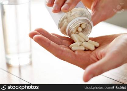 healthcare, medicine, nutritional supplements and people concept - close up of man pouring pills from jar to hand. close up of man pouring pills from jar to hand