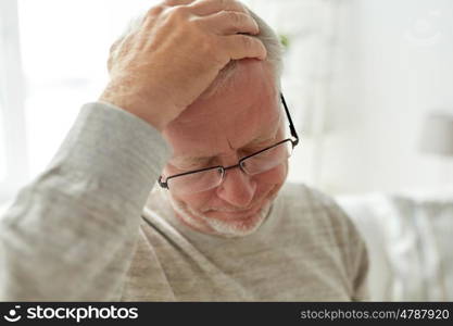 healthcare, pain, stress, age and people concept - senior man suffering from headache at home