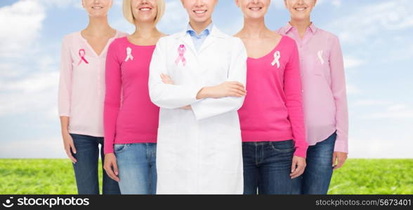 healthcare, people and medicine concept - close up of smiling women in blank shirts with pink breast cancer awareness ribbons over blue sky and grass background