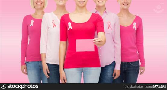 healthcare, people and medicine concept - close up of smiling women in shirts with breast cancer awareness ribbons and blank paper card over pink background
