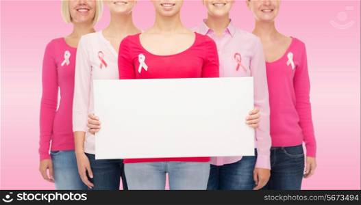 healthcare, people and medicine concept - close up of smiling women in shirts with breast cancer awareness ribbons and blank white board over pink background