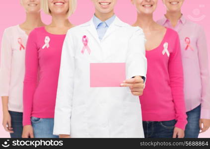 healthcare, people and medicine concept - close up of smiling women in shirts with breast cancer awareness ribbons and blank paper card over pink background