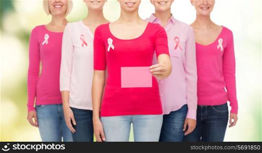 healthcare, people and medicine concept - close up of smiling women in shirts with pink breast cancer awareness ribbons and blank paper card over green background