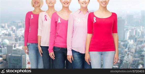 healthcare, people and medicine concept - close up of smiling women in blank shirts with pink breast cancer awareness ribbons over city background