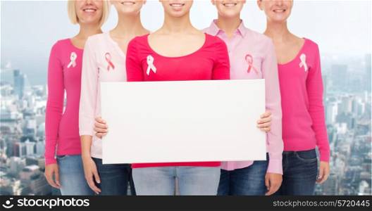 healthcare, people and medicine concept - close up of smiling women in shirts with pink breast cancer awareness ribbons and blank white board over city background