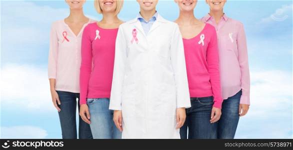 healthcare, people and medicine concept - close up of smiling women in blank shirts with pink breast cancer awareness ribbons over blue sky background