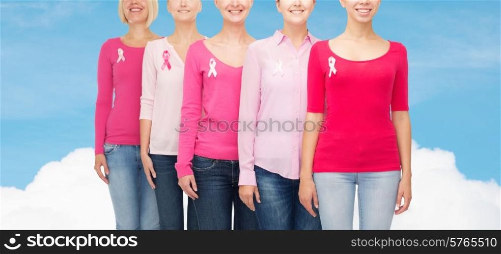 healthcare, people and medicine concept - close up of smiling women in blank shirts with pink breast cancer awareness ribbons over blue sky and white cloud background