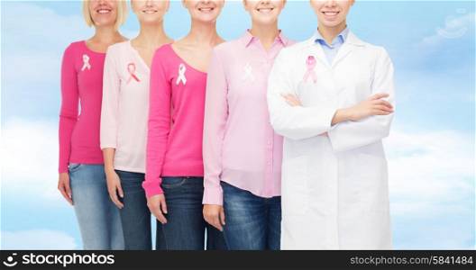 healthcare, people and medicine concept - close up of smiling women in blank shirts with pink breast cancer awareness ribbons over blue sky background