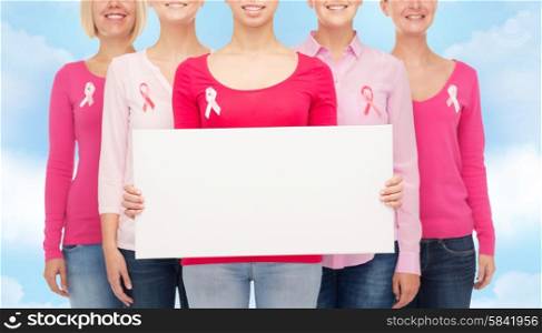 healthcare, people and medicine concept - close up of smiling women in shirts with pink breast cancer awareness ribbons and blank white board over blue sky background