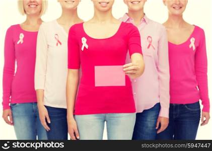 healthcare, people and medicine concept - close up of smiling women in shirts with pink breast cancer awareness ribbons and blank paper card over white background