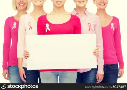 healthcare, people and medicine concept - close up of smiling women in shirts with pink breast cancer awareness ribbons and blank white board over white background