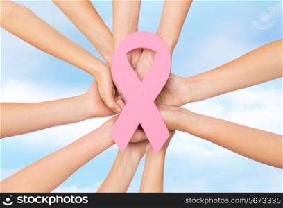 healthcare, people and medicine concept - close up of women hands with paper cancer awareness symbol over blue sky background