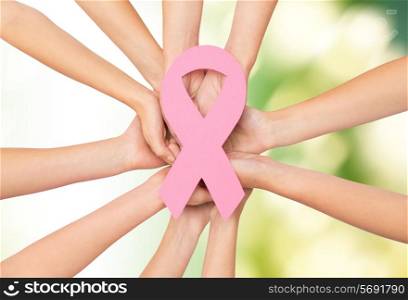 healthcare, people and medicine concept - close up of women hands with paper cancer awareness symbol over green background