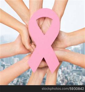 healthcare, people and medicine concept - close up of women hands with paper cancer awareness symbol over city background