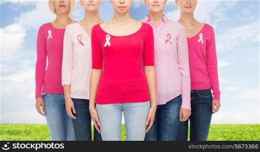 healthcare, people and medicine concept - close up of women in blank shirts with pink breast cancer awareness ribbons over blue sky and grass background
