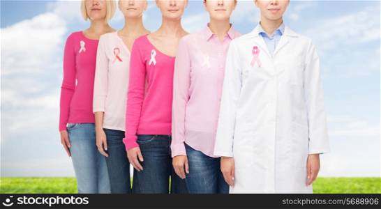 healthcare, people and medicine concept - close up of women in blank shirts with pink breast cancer awareness ribbons over blue sky and grass background