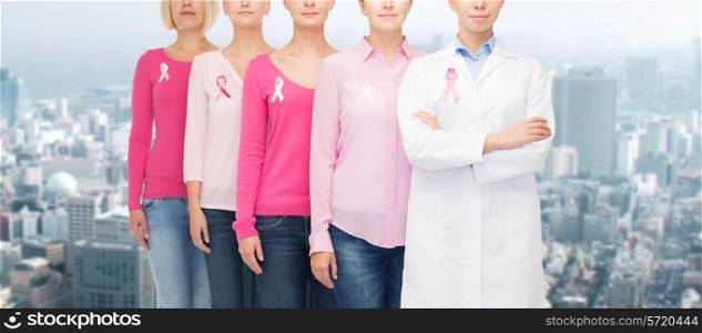 healthcare, people and medicine concept - close up of women in blank shirts with pink breast cancer awareness ribbons over city background