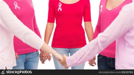 healthcare, people and medicine concept - close up of women in blank shirts with pink breast cancer awareness ribbons holding hands over white background
