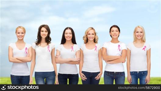 healthcare, people and medicine concept - group of smiling women in blank t-shirts with pink breast cancer awareness ribbons blue sky and grass background